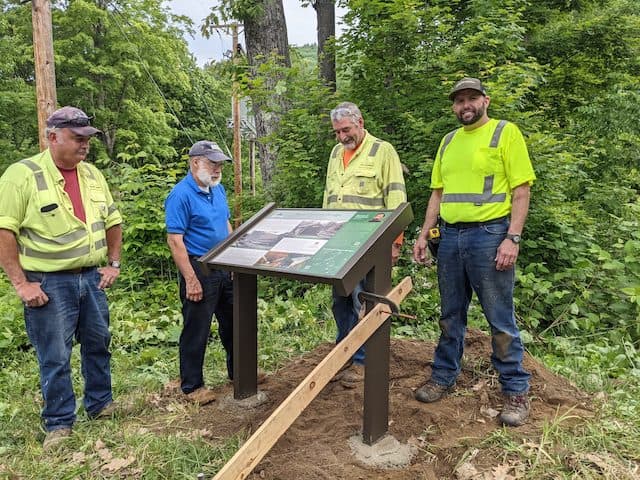 Townshend Highway Department crew and Charlie Marchant, president of Townshend Historical Society, celebrate installation of the final signboard at the west end of Scott Covered Bridge