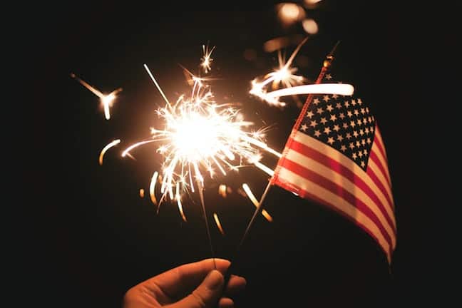 Small American Flag and lit sparkler. Photo by Stephanie McCabe, Unsplash